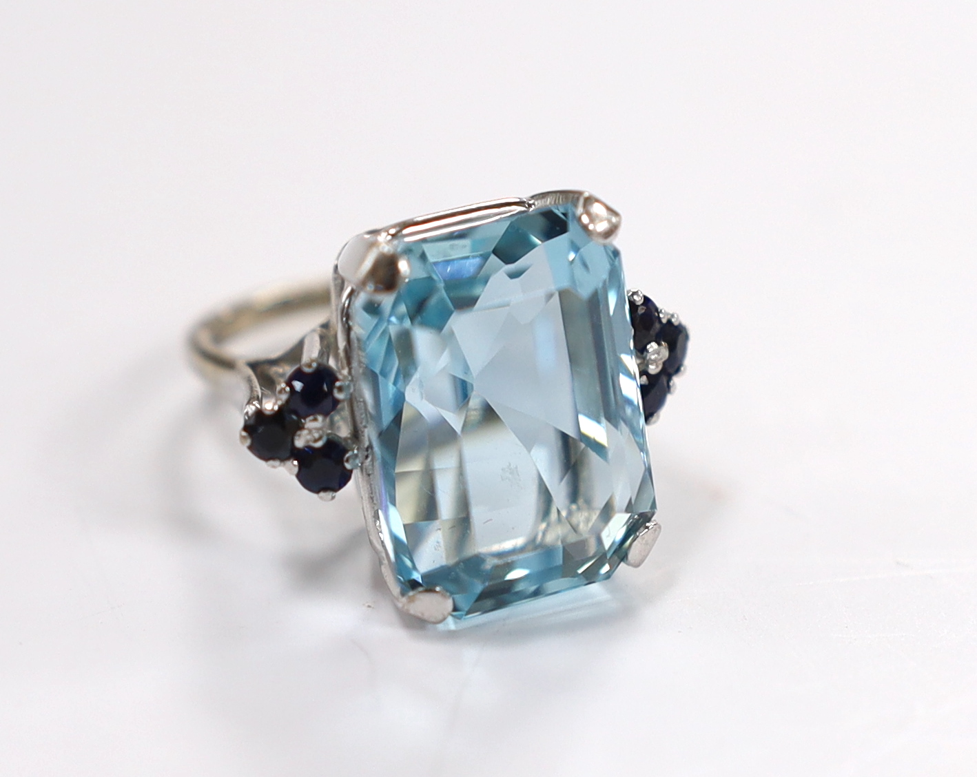 An 18ct white metal and single stone emerald cut aquamarines set dress ring, with six stone sapphire set shoulders, size L, gross weight 11.7 grams.